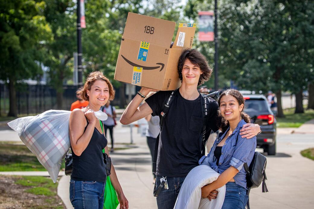 Two students and a parent posing for a picture with moving boxes