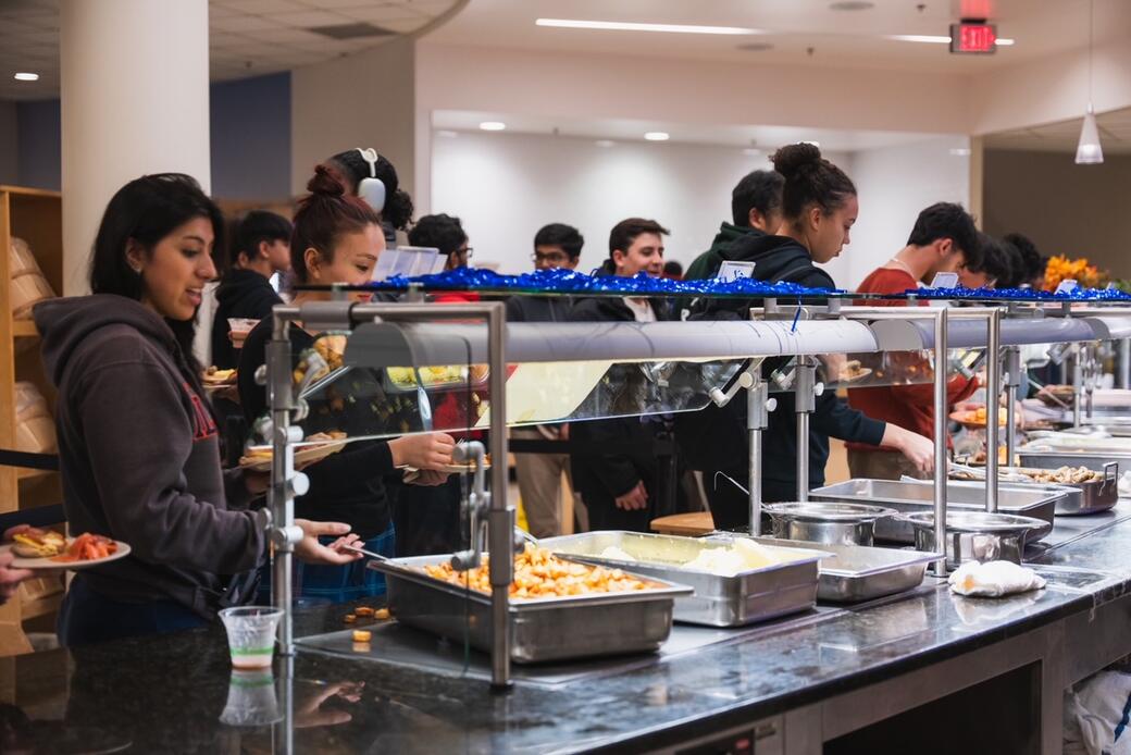The photo shows students in line at a University Housing dining hall filling their plates from a variety of options in front of them.