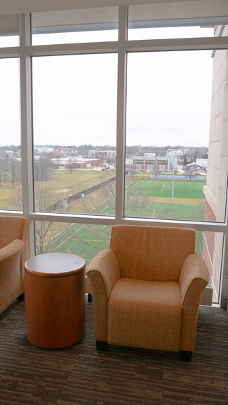 Floor lounge with chair, side table, window looking out onto soccer fields