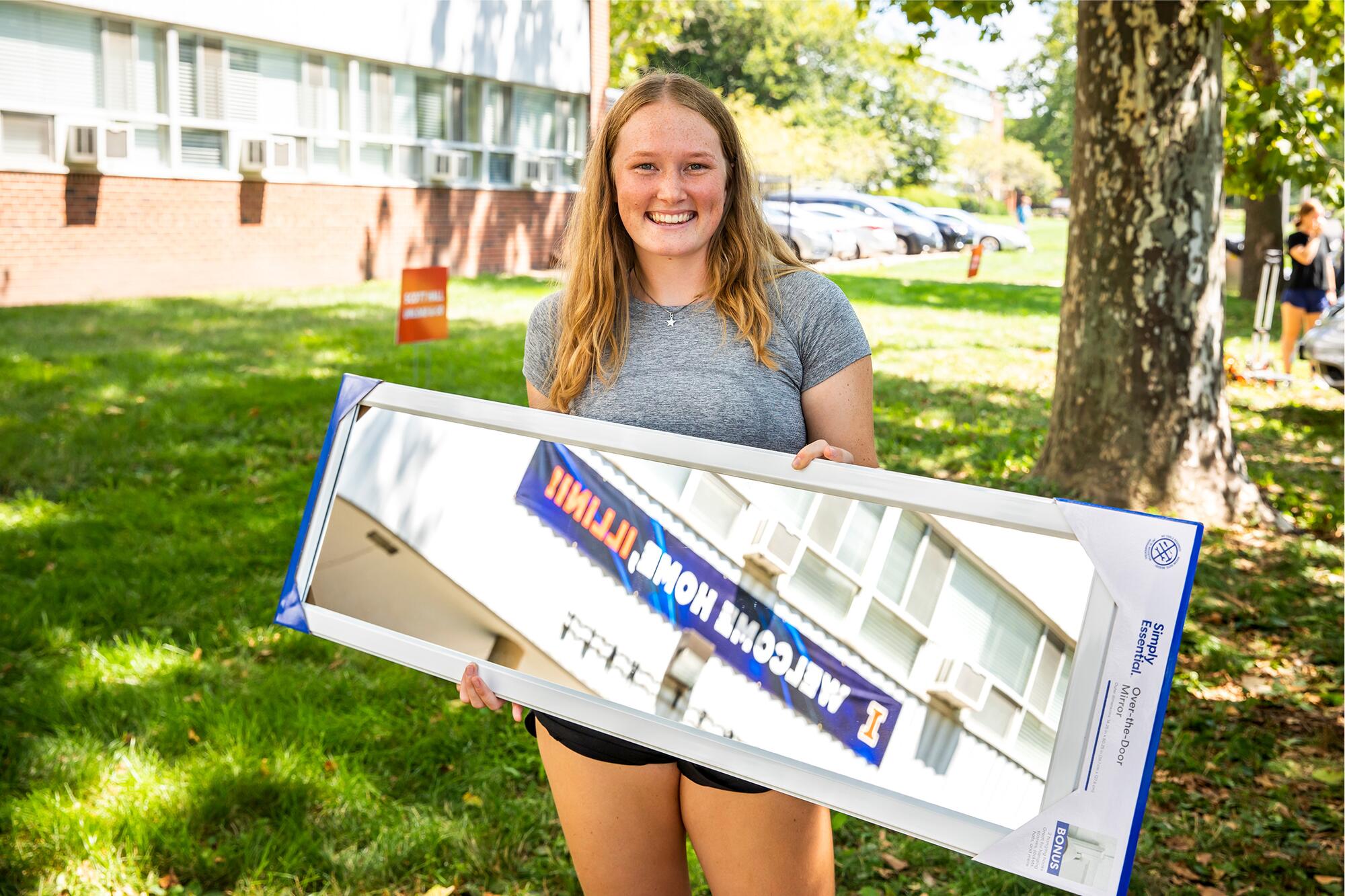 student holds mirror on lawn during move in