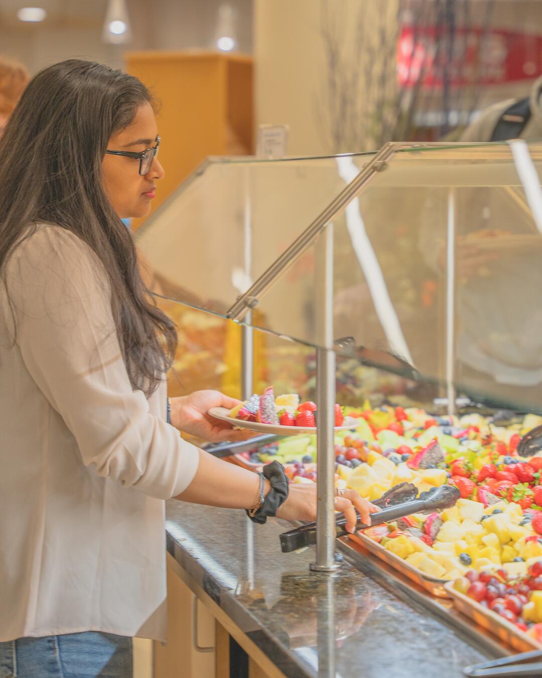 A student is shown filling their plate from a selection of fruit offered in a University Housing dining hall.
