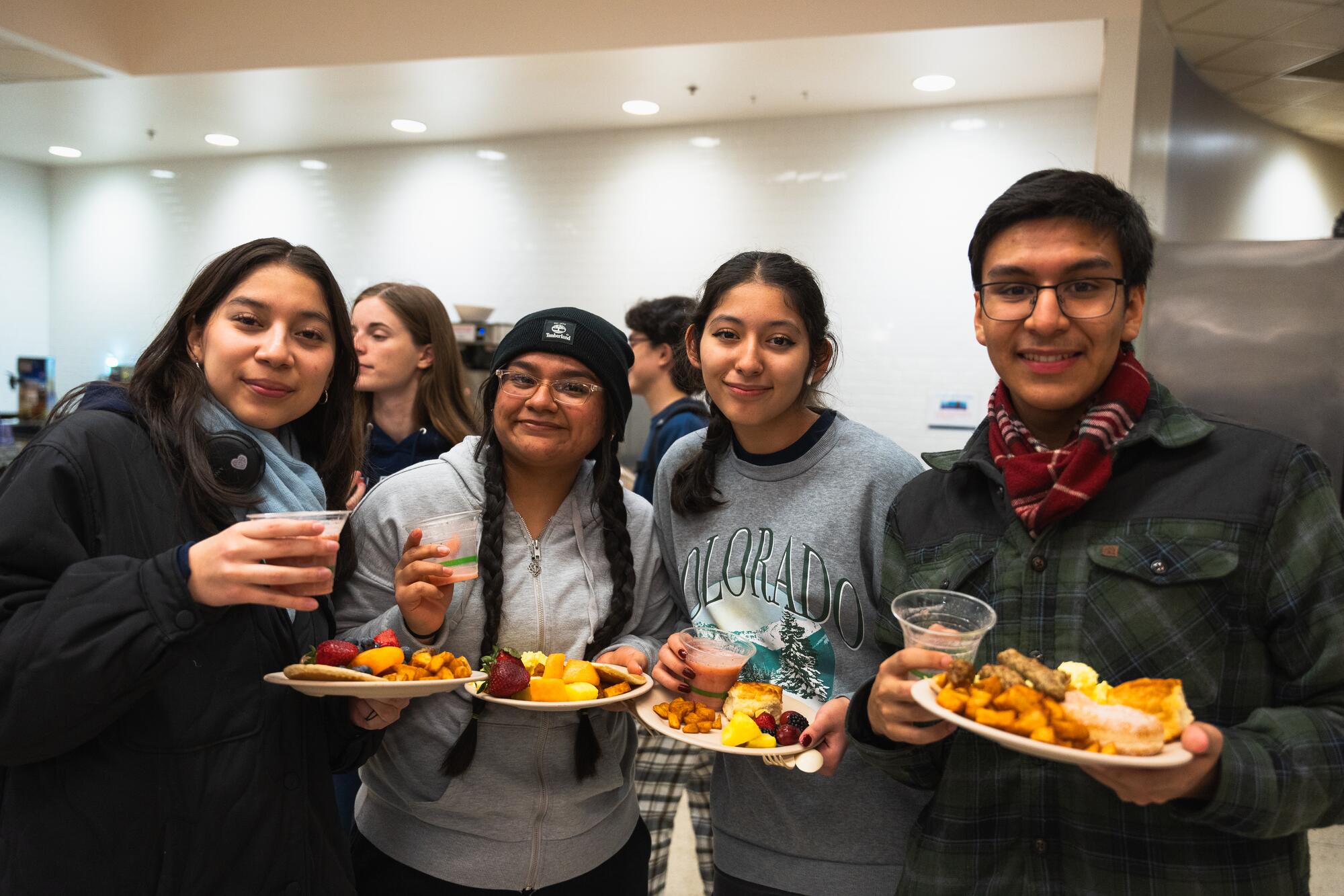Four students with plates full of food pose for a photo in a University Housing dining hall.